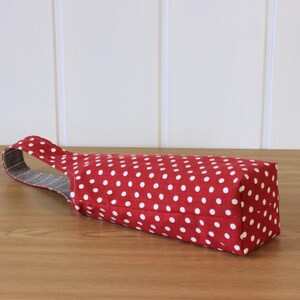 May include: Red fabric wine bottle bag with white polka dots and a gray and white striped handle.