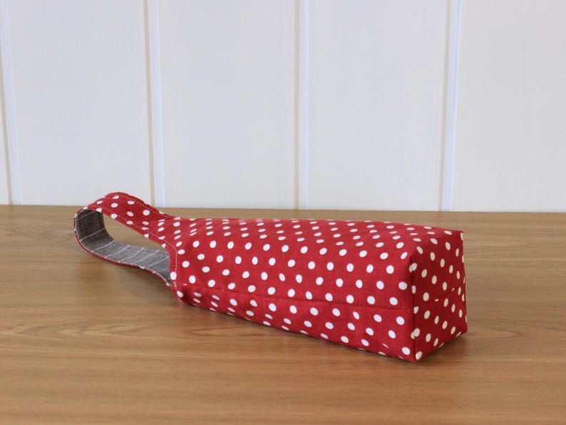 May include: Red fabric wine bottle bag with white polka dots and a gray and white striped handle.