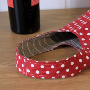 May include: Red and white polka dot fabric wine bottle carrier with a brown and white striped lining.