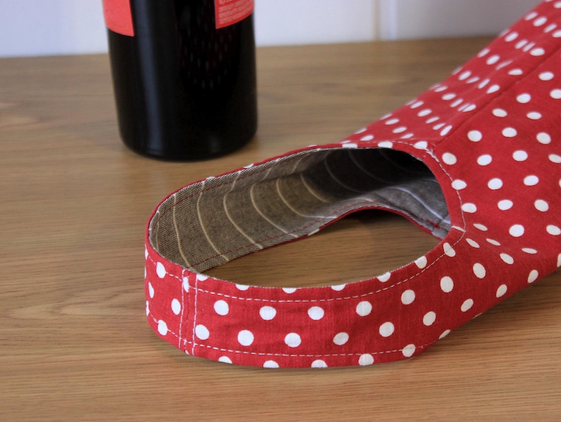 May include: Red and white polka dot fabric wine bottle carrier with a brown and white striped lining.