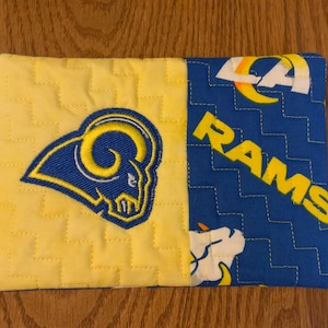 May include: A yellow and blue fabric phone case with the Los Angeles Rams logo. The case is quilted and has a stitched design.