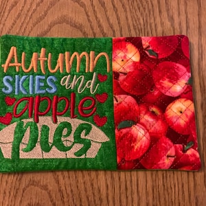 May include: Green quilted pot holder with the text "Autumn skies and apple pies" embroidered in colorful thread. The other side of the pot holder is red with a pattern of red apples.