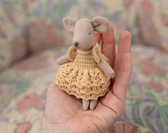 May include: A small gray crocheted mouse wearing a yellow crocheted dress. The mouse is sitting in the palm of a hand.