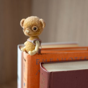 A cute little felt bear can sit on top of a  book and watch the world