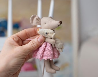 May include: A handmade plush mouse wearing a pink knitted dress and holding a smaller white plush mouse.