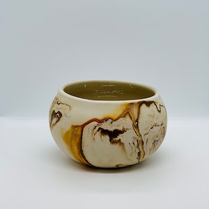 May include: A white ceramic bowl with brown and yellow marbling. The bowl is round and has a slightly flared lip.