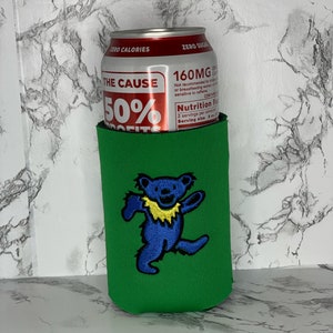 May include: Green can cooler with a blue and yellow dancing bear graphic. The can cooler is wrapped around a silver can with the text "The Cause 50% Profits" and "160MG Caffeine".