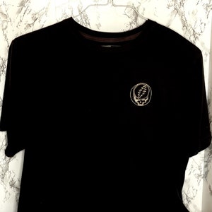May include: Black t-shirt with a white graphic of a smiling face with a lightning bolt on the forehead. The graphic is inside a circle.