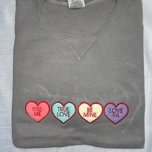 May include: Gray sweatshirt with four embroidered hearts that say "Kiss Me", "True Love", "Be Mine", and "Love Ya".