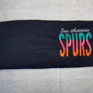 May include: Black t-shirt with "San Antonio SPURS" embroidered in colorful lettering.