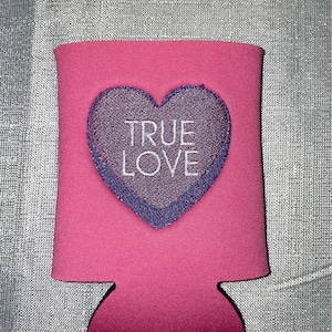 May include: Pink can cooler with a purple heart that says "TRUE LOVE" in white text.