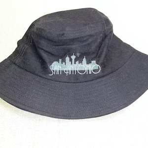 May include: Black bucket hat with a white embroidered skyline and the text "San Antonio" on the front.