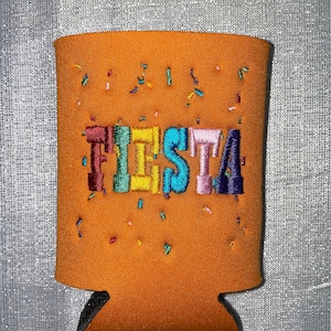 May include: Orange can cooler with the word "FIESTA" embroidered in rainbow colors. The cooler is decorated with confetti.