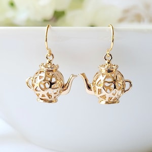 May include: Gold-tone teapot dangle earrings with a delicate, openwork design. The earrings are perfect for adding a touch of whimsy to any outfit.