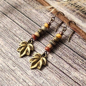 May include: A pair of dangle earrings with gold leaf charms and brown, beige, and yellow beads.
