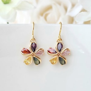 May include: A pair of gold dangle earrings with a flower design. Each flower has five petals with different colored gemstones: purple, pink, orange, yellow, and green.