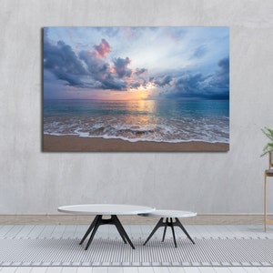 May include: A photograph of a beach scene with a cloudy sky and a sunset over the ocean. The waves are crashing on the shore and the sand is white.
