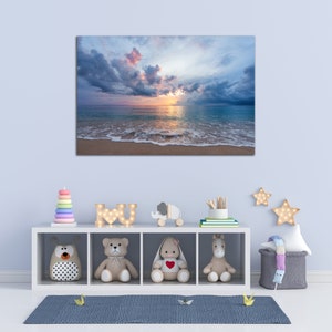 May include: A white shelf unit with four compartments, each containing a different stuffed animal. The top shelf has a wooden elephant toy and a wooden sign that says "I love U". The shelf is against a light blue wall with a canvas print of a beach scene with a sunset and clouds.
