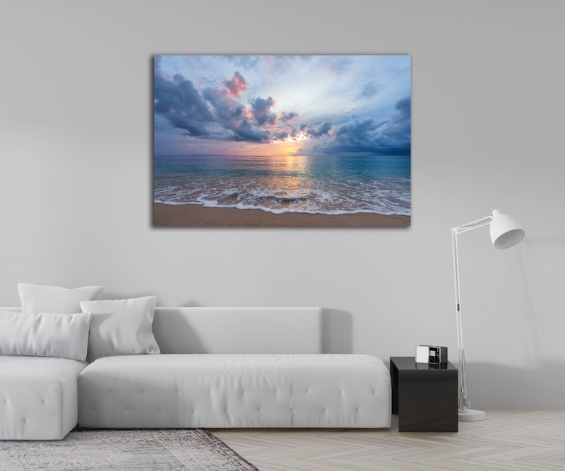 May include: A photograph of a beach scene with a cloudy sky and a sunset over the ocean. The waves are crashing on the shore and the sand is light brown.