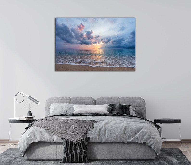 May include: A photograph of a beach scene with a cloudy sky and a calm ocean. The sun is setting behind the clouds, casting a warm glow on the water. The sand is white and the waves are gently lapping at the shore.