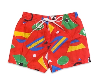 May include: Red swim trunks with a geometric pattern in blue, yellow, and green.