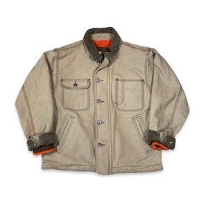 May include: A beige canvas jacket with a corduroy collar and orange lining. The jacket has two large pockets on the front and a button closure.