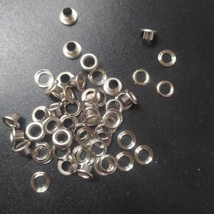 May include: A pile of silver metal eyelets for crafts and leatherworking projects.