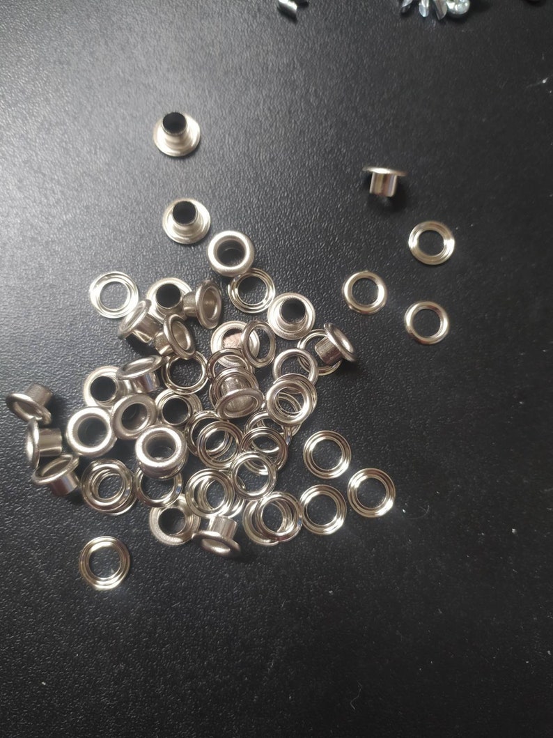 May include: A pile of silver metal eyelets for crafts and leatherworking projects.