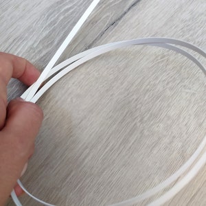 Op de afbeelding: Twee witte plastic strips, &eacute;&eacute;n recht en &eacute;&eacute;n gebogen in een cirkel.