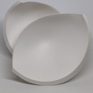 Op de afbeelding: Twee witte schuimrubberen bh-cups, ontworpen om lift en vorm te geven. De cups zijn glad en naadloos, met een afgeronde vorm.