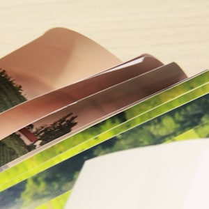Può includere: Una pila di fotografie con un'immagine di paesaggio verde e marrone in basso. La fotografia in alto è di colore marrone chiaro.