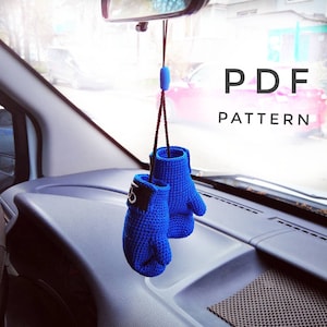 Puede incluir: Un par de guantes de boxeo de crochet azul colgando de un espejo retrovisor en un coche. Los guantes tienen ribetes negros y letras blancas. El texto "PDF PATTERN" es visible en la esquina superior derecha de la imagen.