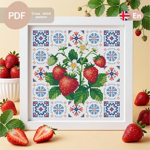 Peut inclure: Un modèle de point de croix encadré représentant un groupe central de fraises rouges avec des feuilles vertes et des fleurs blanches, entouré d'une bordure géométrique de carreaux bleus, rouges et blancs dans un cadre carré blanc.
