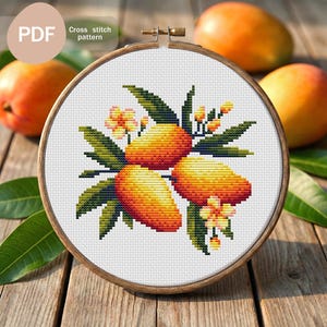 May include: A cross-stitch pattern of three mangoes with green leaves and small orange flowers, set in a wooden embroidery hoop. The text "PDF" and "Cross stitch pattern" are in the upper left.