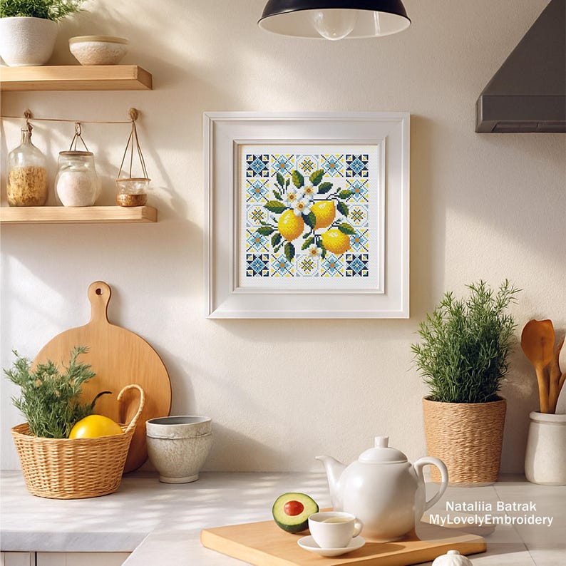 May include: A framed cross-stitch artwork featuring lemons, white blossoms, and green leaves. The artwork is set against a blue and yellow geometric pattern. The kitchen scene includes a teapot, teacup, and a basket with a lemon.