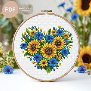 May include: A cross-stitch pattern of a heart-shaped floral arrangement featuring sunflowers and blue flowers. The design is set within a wooden embroidery hoop. The text "PDF" and "Cross stitch pattern" are visible.