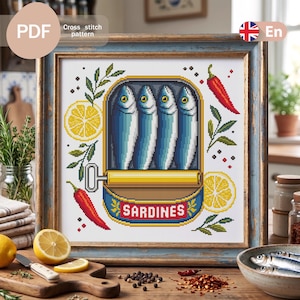 Puede incluir: Un patrón de punto de cruz que muestra una lata rectangular con cuatro sardinas azules y plateadas con una anilla amarilla. El diseño incluye dos rodajas de limón amarillo, dos chiles rojos y hierbas verdes sobre un fondo blanco.