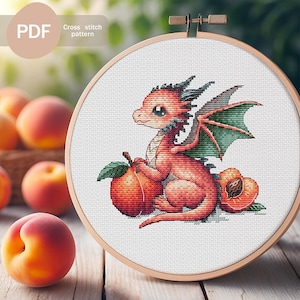 Puede incluir: Un patrón de punto de cruz en un bastidor de madera presenta un dragón rojo con alas verdes, junto a un melocotón. El texto "PDF" y "Cross stitch pattern" están en la esquina superior izquierda. Melocotones en el fondo.