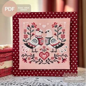 Può includere: Modello di punto croce con due colombe bianche con accenti rossi e blu, circondate da motivi floreali rossi e verdi su uno sfondo rosa. Il modello è incorniciato in un tessuto rosso con pois bianchi. Il testo "Cross stitch pattern" e "Natalia Batrak MyLovelyEmbroidery" è visibile.