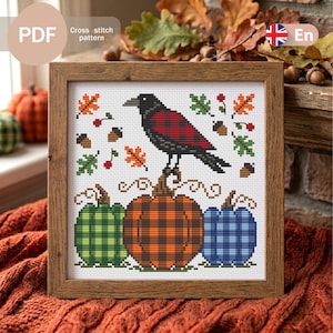 Op de afbeelding: Een kruissteekpatroon met een zwarte kraai met een rood geruite vleugel op een grote oranje geruite pompoen. Het ontwerp bevat een groene geruite pompoen, een blauwe geruite pompoen, herfstbladeren, eikels en kleine rode bessen.