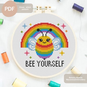 Puede incluir: Patrón de punto de cruz con una abeja linda con alas de arcoíris y un arcoíris encima. El texto "BEE YOURSELF" está debajo de la abeja.