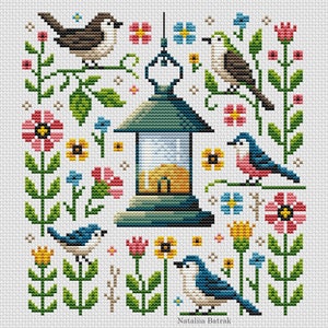 May include: Cross stitch pattern featuring a lantern with a yellow glow, surrounded by colorful flowers and birds. The birds are blue, brown, and pink, and the flowers are pink, yellow, and blue. The pattern is titled "Natalia Batrak".