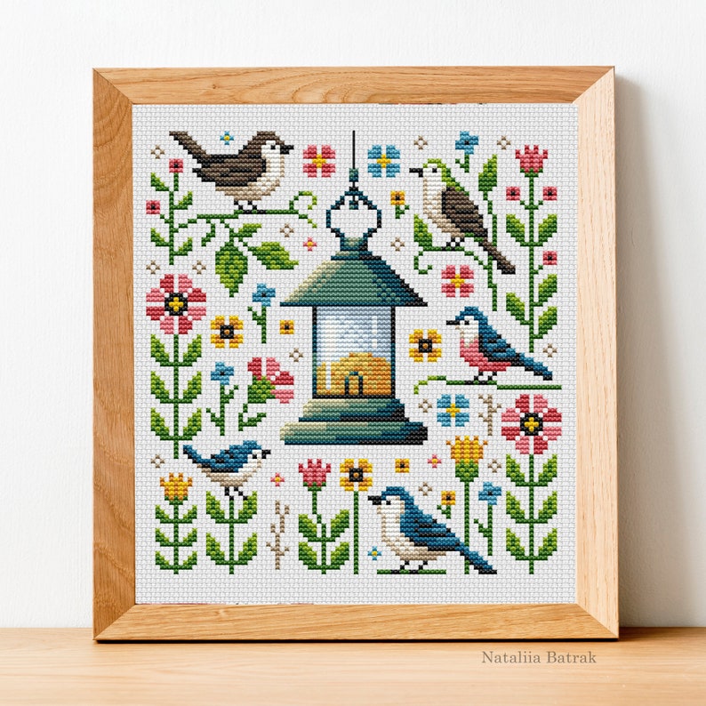 May include: Cross stitch pattern featuring a lantern with a blue roof and yellow windows surrounded by colorful flowers and birds. The birds are blue, red, and brown with yellow beaks. The flowers are pink, yellow, and blue. The pattern is on a white background.
