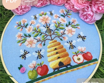 May include: A cross stitch pattern PDF featuring a beehive with a tree full of pink blossoms and bees flying around. The beehive is made of yellow and brown thread and the tree is made of green and brown thread. The bees are made of yellow and black thread. The background is a light blue color. The text "Cross stitch pattern" is written in black text on a peach background. The text "PDF" is written in white text on a peach background.