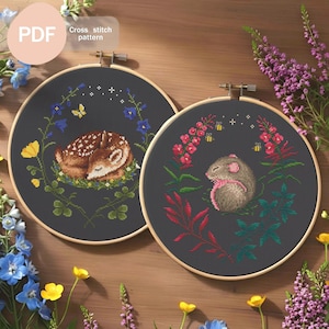 May include: Two cross-stitch patterns in wooden hoops. One features a sleeping fawn surrounded by bluebells and butterflies. The other depicts a mouse with a pink bow, surrounded by flowers and bees. The text "Cross stitch pattern" is visible.