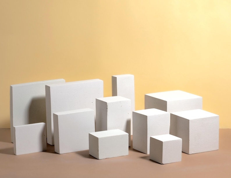 Pode incluir: Uma variedade de blocos brancos retangulares e em forma de cubo de v&aacute;rios tamanhos. Os blocos est&atilde;o dispostos sobre uma superf&iacute;cie marrom contra um fundo amarelo claro, criando uma est&eacute;tica minimalista.