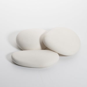 May include: Three smooth, white, oval-shaped stones are arranged on a white background. The stones have a matte finish and varying sizes, with soft, rounded edges. The composition suggests a natural, minimalist aesthetic.