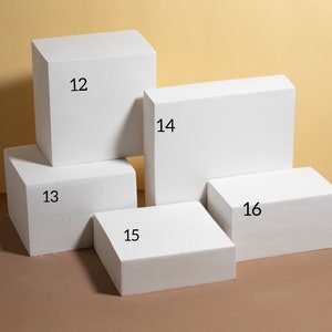Pode incluir: Uma cole&ccedil;&atilde;o de blocos de exibi&ccedil;&atilde;o geom&eacute;tricos brancos de v&aacute;rios tamanhos. Os blocos est&atilde;o dispostos em uma composi&ccedil;&atilde;o visualmente atraente, com os n&uacute;meros 12, 13, 14, 15 e 16 vis&iacute;veis nos blocos. O fundo &eacute; de cor bege neutra.
