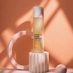 Puede incluir: Una botella de vidrio transparente de t&oacute;nico facial de vitamina C y prop&oacute;leo con tapa blanca, colocada sobre un pedestal blanco texturizado. La botella est&aacute; etiquetada con informaci&oacute;n del producto. El fondo es de color melocot&oacute;n c&aacute;lido con un dise&ntilde;o geom&eacute;trico.