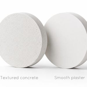 Puede incluir: Dos objetos circulares, uno con una superficie de hormig&oacute;n texturizado y otro con una superficie de yeso liso. El texto de abajo dice "Textured concrete" y "Smooth plaster".